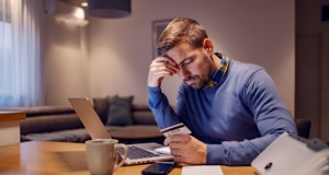 A worried man looking at his credit card with no invoice and having troubles with payment while sitting at home.
