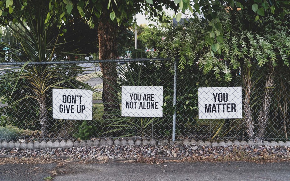 Three white signs, saying,' don't give up', 'you are not alone' and 'you matter', attached to a metal fence