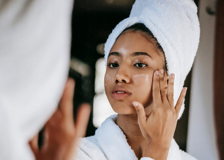 woman in mirror applying cream on face in bathrobe