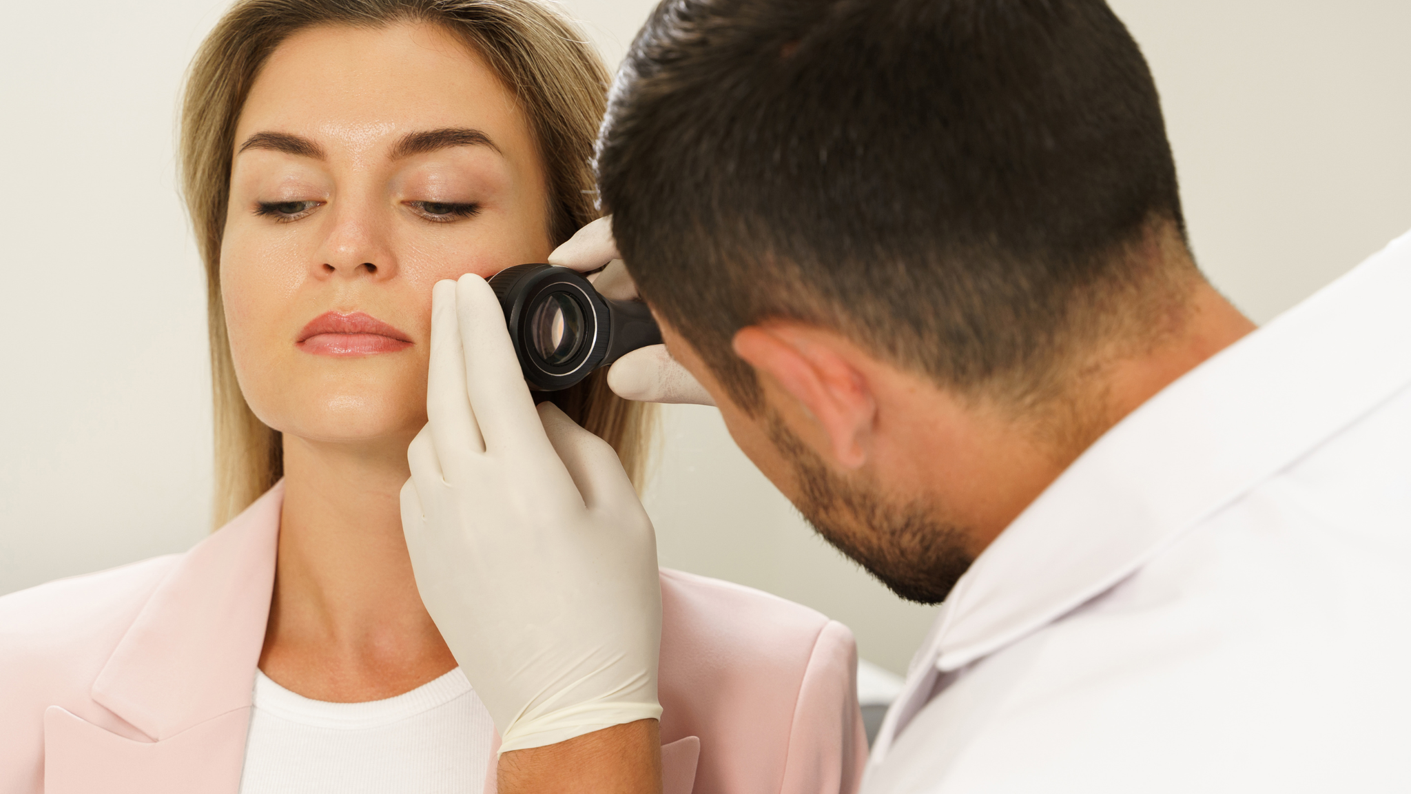 Dermatologist measuring facial skin hydration with a handheld skin analysis device during a professional skincare assessment.